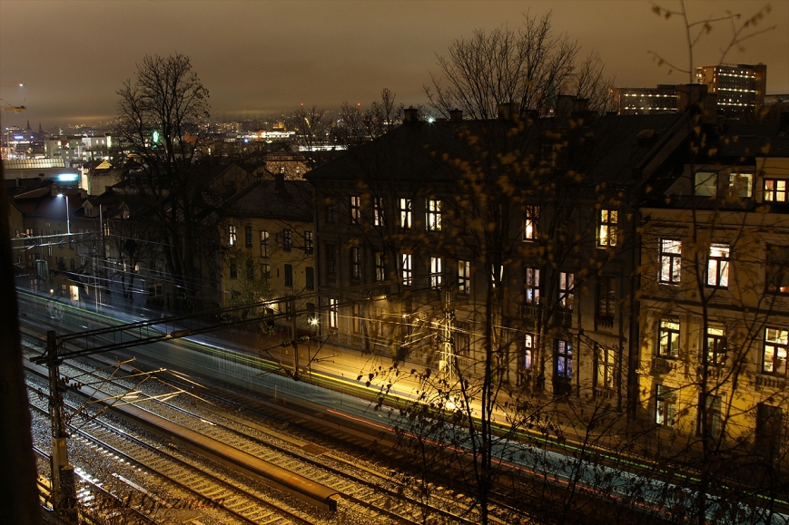 Light-trails from train photographing in low-light, with the cityscape of a rainy Oslo in the background. 